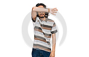 Young hispanic man wearing casual clothes covering eyes with arm, looking serious and sad