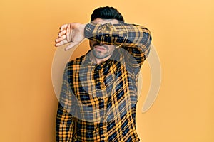 Young hispanic man wearing casual clothes covering eyes with arm, looking serious and sad
