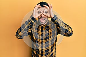 Young hispanic man wearing casual clothes doing ok gesture like binoculars sticking tongue out, eyes looking through fingers