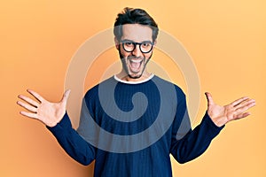 Young hispanic man wearing casual clothes and glasses celebrating victory with happy smile and winner expression with raised hands