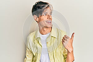 Young hispanic man wearing casual clothes pointing thumb up to the side smiling happy with open mouth