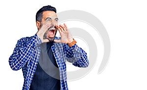 Young hispanic man wearing casual clothes shouting angry out loud with hands over mouth