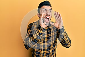 Young hispanic man wearing casual clothes shouting angry out loud with hands over mouth