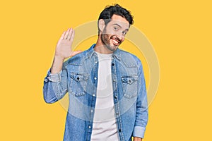 Young hispanic man wearing casual clothes waiving saying hello happy and smiling, friendly welcome gesture