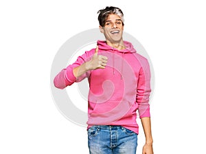 Young hispanic man wearing casual pink sweatshirt doing happy thumbs up gesture with hand