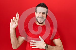 Young hispanic man wearing casual red t shirt smiling swearing with hand on chest and fingers up, making a loyalty promise oath