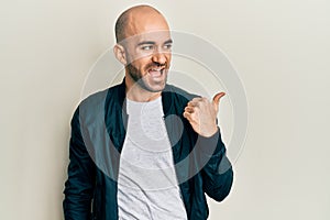 Young hispanic man wearing casual sporty jacket pointing thumb up to the side smiling happy with open mouth