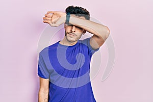 Young hispanic man wearing casual t shirt covering eyes with arm, looking serious and sad