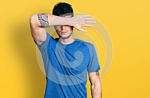 Young hispanic man wearing casual t shirt covering eyes with arm, looking serious and sad
