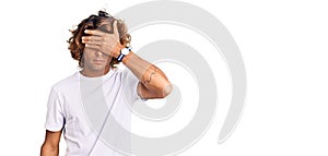 Young hispanic man wearing casual white tshirt covering eyes with hand, looking serious and sad