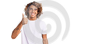 Young hispanic man wearing casual white tshirt doing happy thumbs up gesture with hand