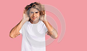 Young hispanic man wearing casual white tshirt trying to hear both hands on ear gesture, curious for gossip