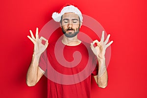 Young hispanic man wearing christmas hat relax and smiling with eyes closed doing meditation gesture with fingers