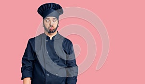 Young hispanic man wearing cooker uniform making fish face with lips, crazy and comical gesture