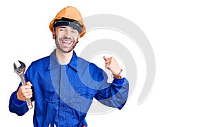 Young hispanic man wearing electrician uniform holding wrench screaming proud, celebrating victory and success very excited with