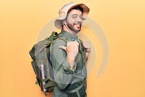 Young hispanic man wearing explorer hat and bakcpack smiling happy pointing with hand and finger