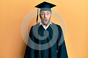 Young hispanic man wearing graduation cap and ceremony robe afraid and shocked with surprise expression, fear and excited face