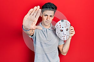 Young hispanic man wearing hockey mask with open hand doing stop sign with serious and confident expression, defense gesture