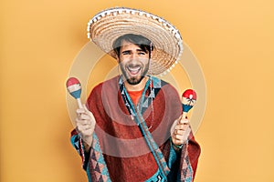 Young hispanic man wearing mexican hat holding maracas smiling and laughing hard out loud because funny crazy joke