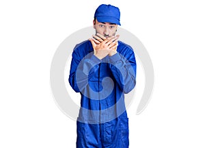 Young hispanic man wearing painter uniform shocked covering mouth with hands for mistake