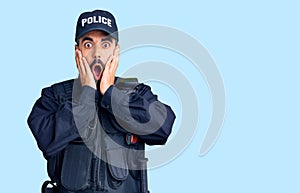 Young hispanic man wearing police uniform afraid and shocked, surprise and amazed expression with hands on face