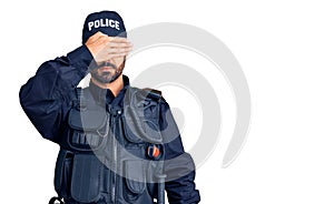 Young hispanic man wearing police uniform covering eyes with hand, looking serious and sad