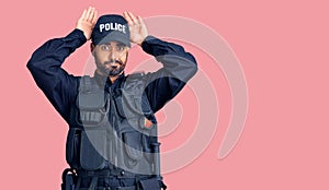 Young hispanic man wearing police uniform doing bunny ears gesture with hands palms looking cynical and skeptical
