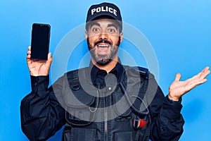 Young hispanic man wearing police uniform holding smartphone celebrating achievement with happy smile and winner expression with