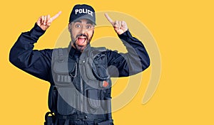 Young hispanic man wearing police uniform smiling amazed and surprised and pointing up with fingers and raised arms