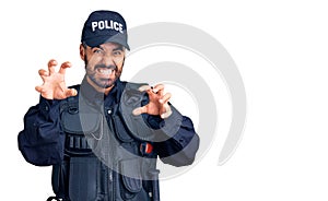 Young hispanic man wearing police uniform smiling funny doing claw gesture as cat, aggressive and sexy expression