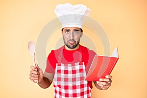 Young hispanic man wearing professional baker apron reading cooking recipe book depressed and worry for distress, crying angry and