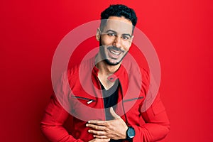 Young hispanic man wearing red leather jacket smiling and laughing hard out loud because funny crazy joke with hands on body