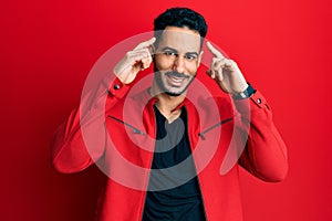 Young hispanic man wearing red leather jacket smiling pointing to head with both hands finger, great idea or thought, good memory