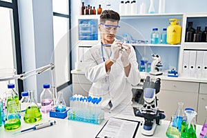 Young hispanic man wearing scientist uniform writing on test tube at laboratory