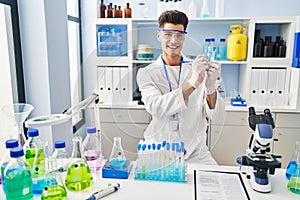 Young hispanic man wearing scientist uniform writing on test tube at laboratory