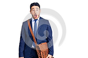 Young hispanic man wearing suit and leather bag scared and amazed with open mouth for surprise, disbelief face