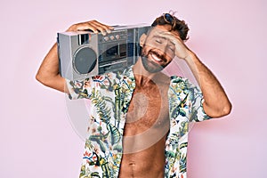 Young hispanic man wearing summer clothes holding boombox, listening to music smiling with hands on chest, eyes closed with