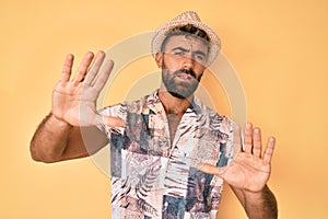 Young hispanic man wearing summer hat afraid and terrified with fear expression stop gesture with hands, shouting in shock