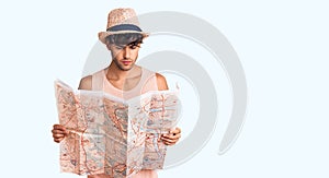 Young hispanic man wearing summer hat holding map thinking attitude and sober expression looking self confident