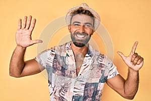 Young hispanic man wearing summer hat showing and pointing up with fingers number seven while smiling confident and happy