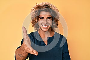 Young hispanic man wearing summer hat smiling friendly offering handshake as greeting and welcoming