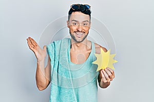 Young hispanic man wearing summer style holding yellow sun celebrating victory with happy smile and winner expression with raised