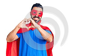 Young hispanic man wearing super hero costume smiling in love showing heart symbol and shape with hands