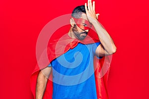 Young hispanic man wearing super hero costume surprised with hand on head for mistake, remember error