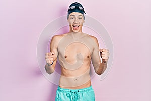 Young hispanic man wearing swimwear and swimmer glasses celebrating surprised and amazed for success with arms raised and open