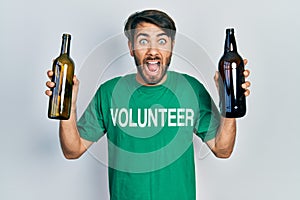 Young hispanic man wearing volunteer t shirt holding recycling bottle glass celebrating crazy and amazed for success with open