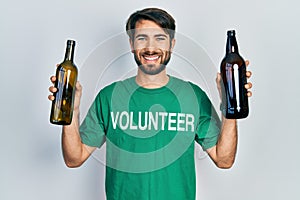 Young hispanic man wearing volunteer t shirt holding recycling bottle glass smiling with a happy and cool smile on face