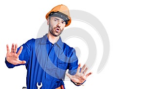 Young hispanic man wearing worker uniform doing stop gesture with hands palms, angry and frustration expression