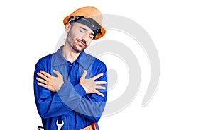 Young hispanic man wearing worker uniform hugging oneself happy and positive, smiling confident