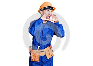 Young hispanic man wearing worker uniform shouting angry out loud with hands over mouth